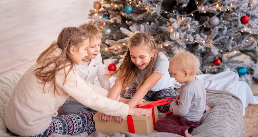 Children opening a gift in the family room next to a Christmas tree.